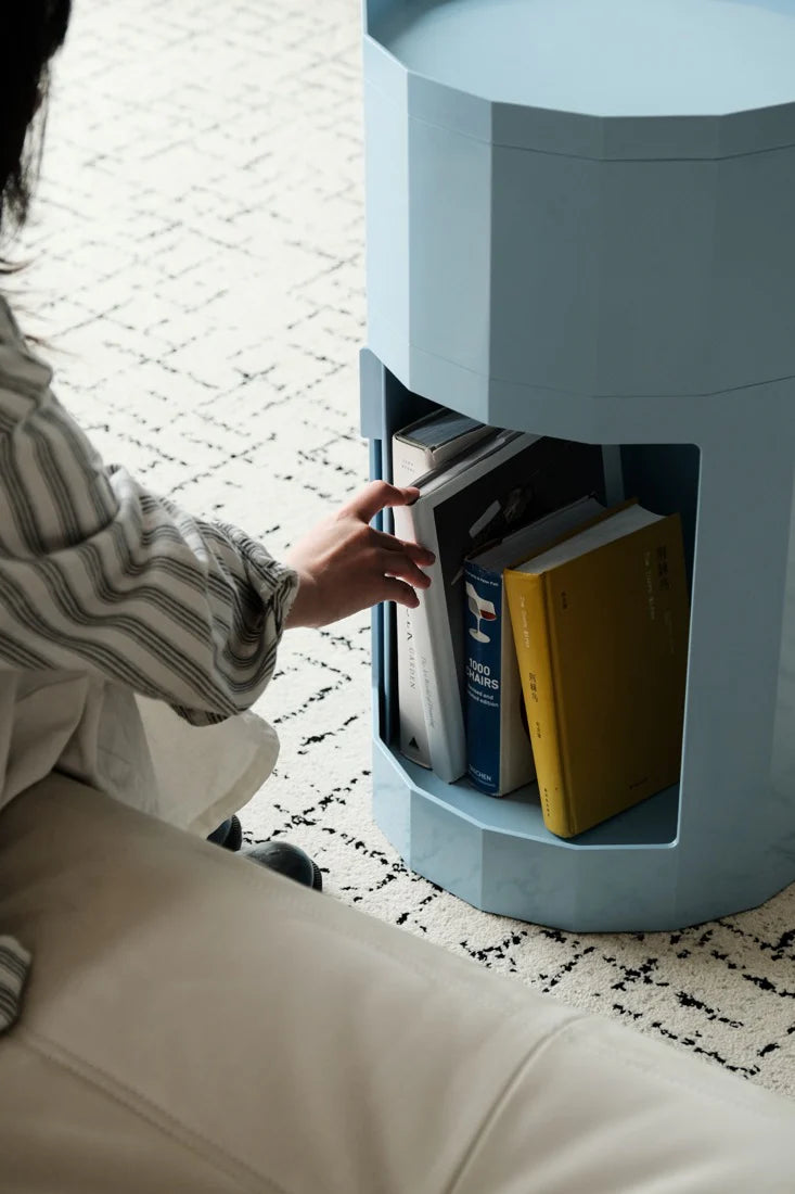 Person reaching into a small blue shelf to retrieve books on a patterned floor.