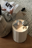 Person reading a book on a couch with a side table featuring a can and lamp.