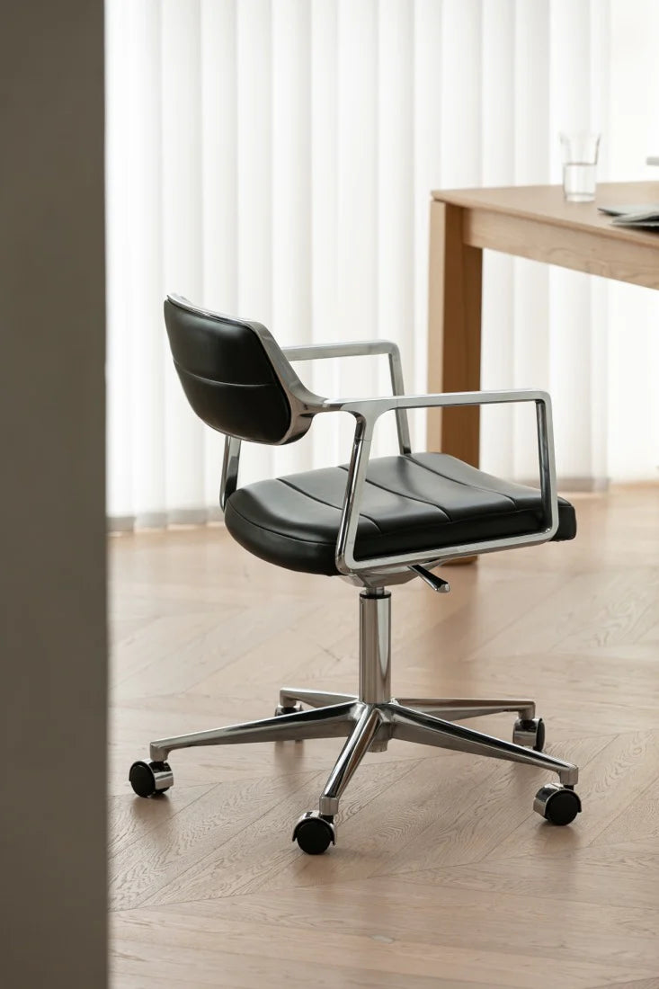Black office chair with chrome base in a minimalistic room with a desk and curtains.