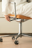 Person sitting on a modern office chair with wooden seat and metal frame.