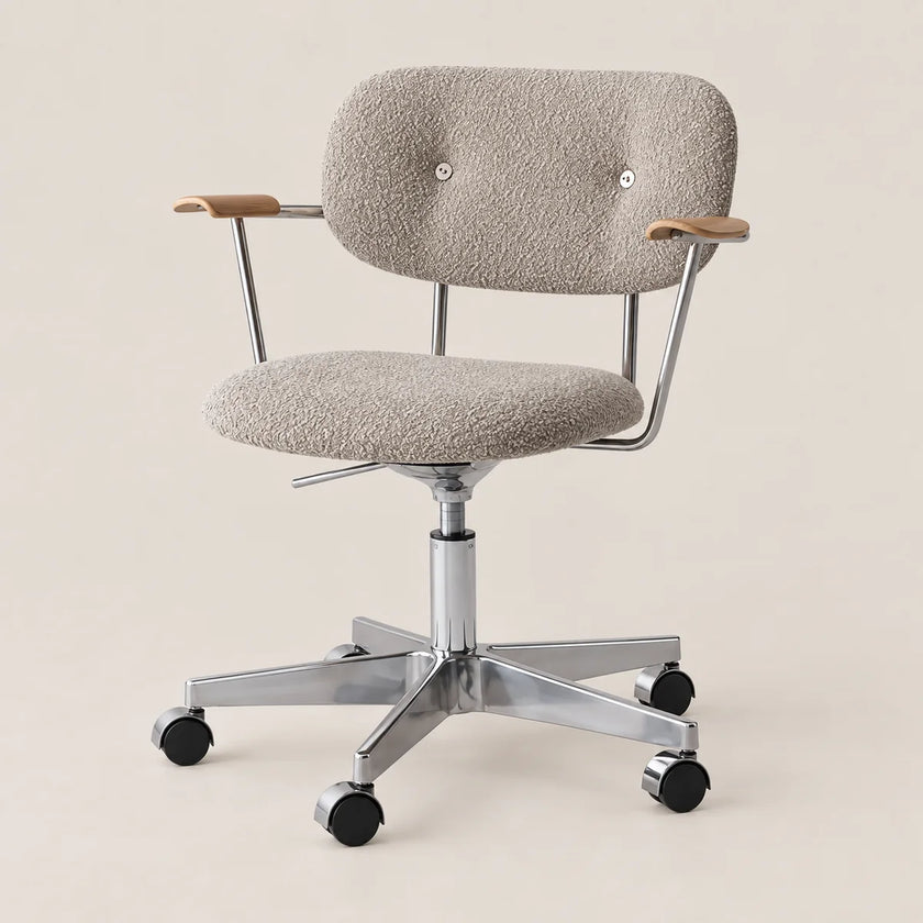 A modern office chair with a textured light beige bouclé upholstered seat and backrest, featuring light wood armrest caps, a chrome metal frame, and black caster wheels, set against a solid light beige background.