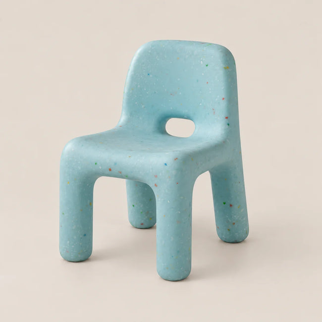 A light blue molded chair with multicolored flecks throughout, featuring a cutout in the center of the backrest, set against a solid beige background.