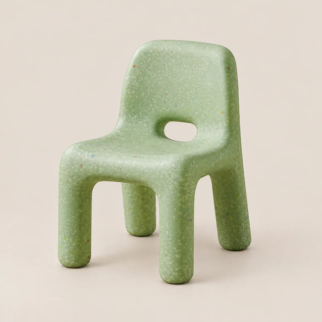 A small molded chair made from speckled light green material, shown on a plain warm beige studio background.