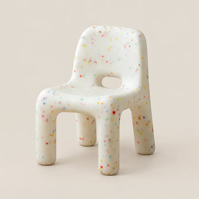A small molded chair with a terrazzo-style speckled pattern in multiple colors on an off-white base, photographed against a solid light beige background.