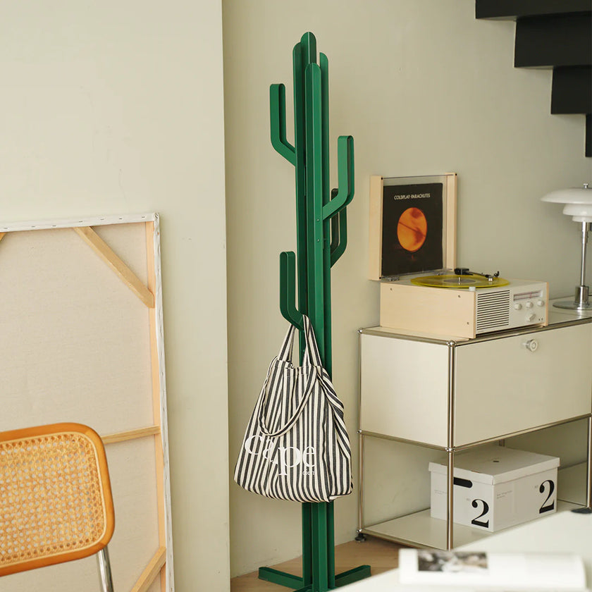 Green cactus-shaped coat rack with a striped bag on a beige wall.