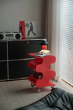 Red side table with books and glasses next to a black cabinet in a room with a window.