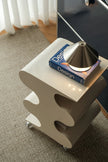 Small white side table with a book titled 'Design' and a metallic object on top, in a room setting.