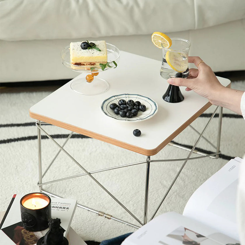 Person holding a glass of water with lemon slices on a small white table with food items.