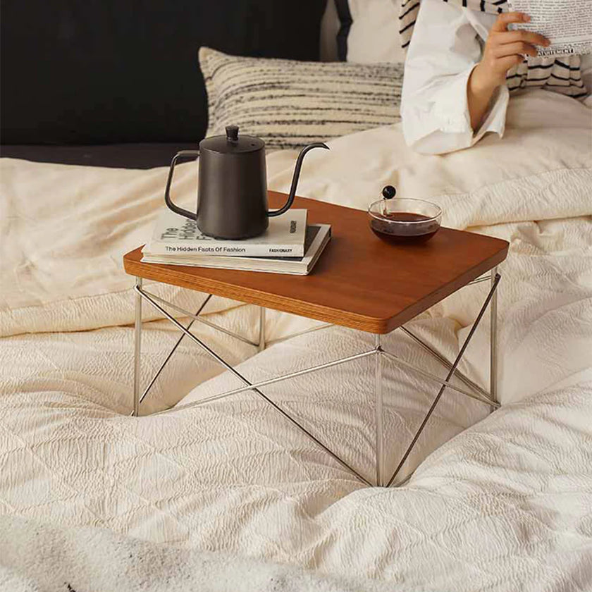 Small wooden table with a teapot, books, and a glass on a bed.