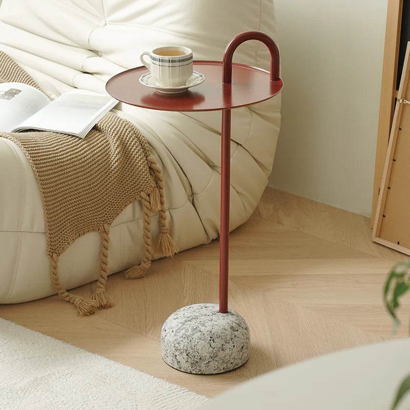 Small round side table with red top and marble base next to a sofa with a blanket and coffee cup.