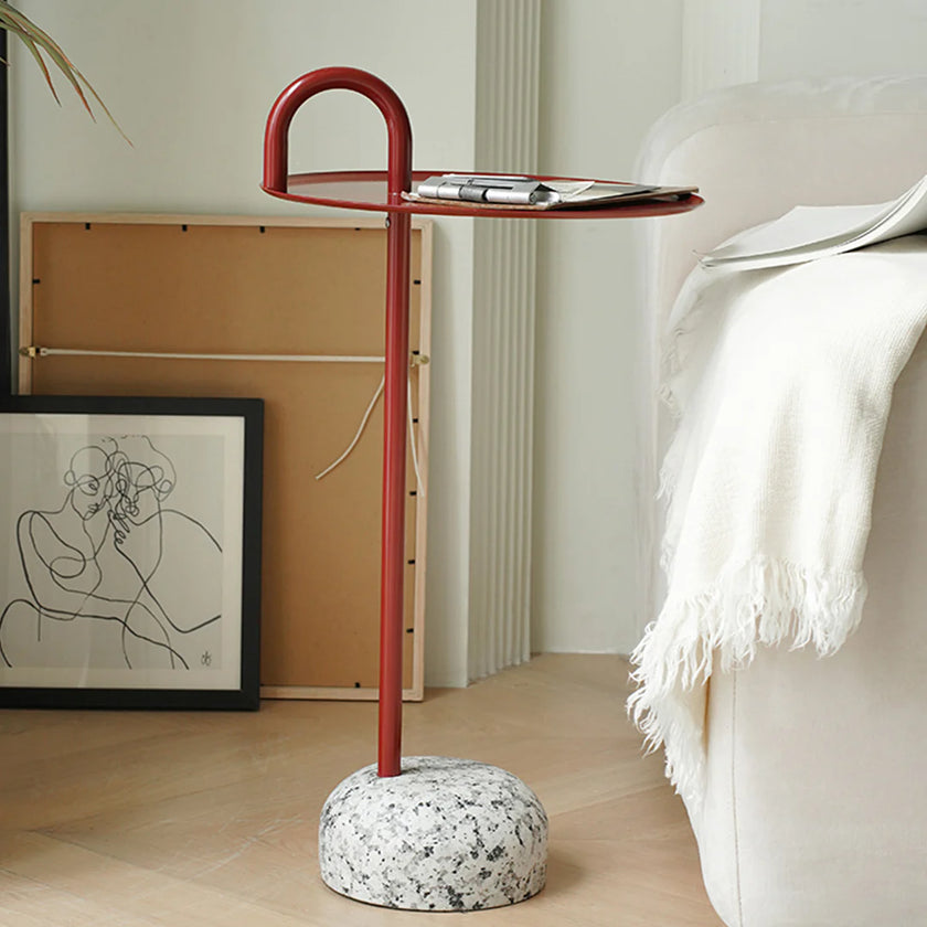 Modern side table with red metal stand and white marble base in a living room setting.