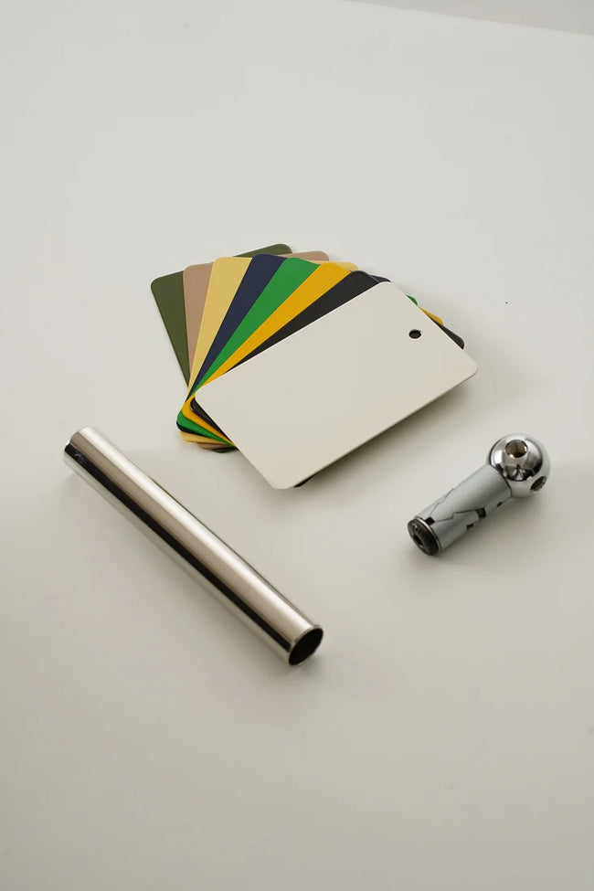 Color swatch card with a metal rod and a small metallic object on a light gray background