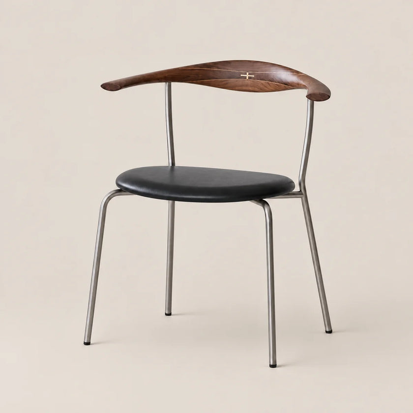 A mid-century modern dining chair featuring a curved dark wood backrest with a small gold cross in the center, a black upholstered seat, and a slim silver metal frame, set against a solid beige background.