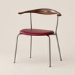 A mid-century modern dining chair featuring a curved dark wood backrest with a small cross inlay, a deep burgundy upholstered seat, and a slim silver metal frame, set against a solid light beige background.
