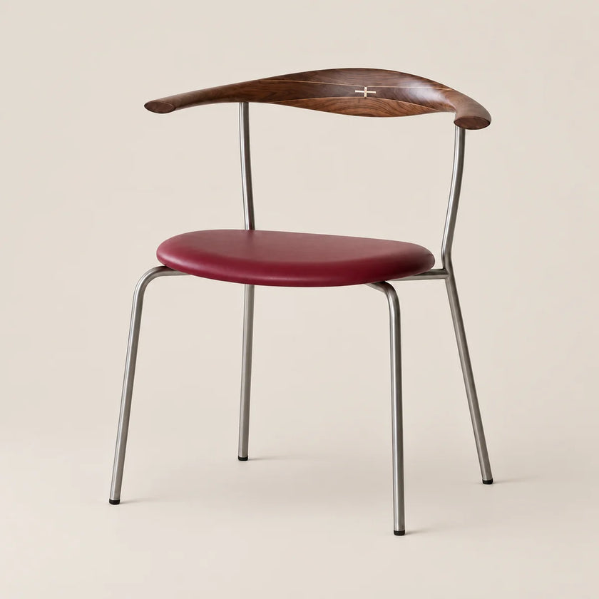 A mid-century modern dining chair featuring a curved dark wood backrest with a small cross inlay, a deep burgundy upholstered seat, and a slim silver metal frame, set against a solid light beige background.