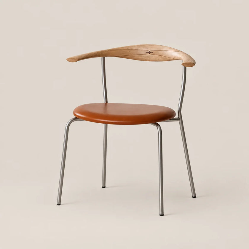 A mid-century modern dining chair featuring a curved natural wood backrest, a round cognac brown leather seat, and a slim silver metal frame, set against a solid warm beige background.