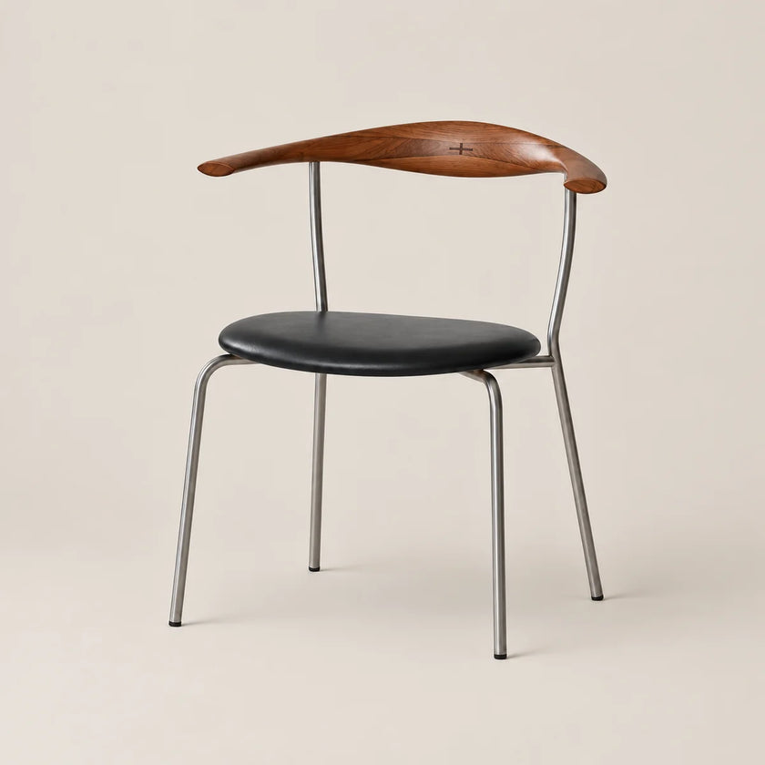 A mid-century modern dining chair featuring a curved wooden armrest, a black leather seat cushion, and a slim silver metal frame, set against a solid warm beige background.