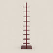 A tall, narrow multi-tier display stand with a central vertical pole and multiple flat horizontal shelves, finished in a dark reddish-brown color, set against a solid light beige background.