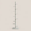 A minimalist, multi-tiered shelving unit or cat tree stand in a light gray finish, featuring a central vertical pole with several horizontal shelves and a square base, set against a solid beige background.