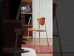 A modern dining chair featuring a curved, light-wood seat and a distinctively shaped backrest with a single circular cutout, supported by a sleek, tubular chrome metal frame.