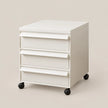 A white three-drawer rolling file cabinet with black caster wheels, shown on a solid light beige background.