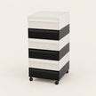 A 6-drawer rolling storage cabinet with a modern striped design in white and black, featuring a white top surface and black caster wheels, shown on a light beige studio background.