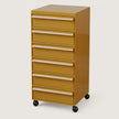 A six-drawer rolling file cabinet in a warm mustard yellow finish with silver metal drawer pulls and black caster wheels, shown on a plain light beige studio background.