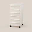 An off-white rolling storage cabinet with eight drawers and black caster wheels, shown on a solid beige background.