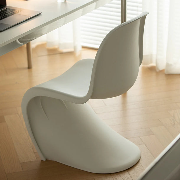 Modern white chair in a minimalistic room with a desk and laptop.