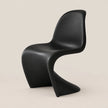 A modern sculptural black chair with a curved shell seat and integrated base, photographed against a plain warm beige studio background.