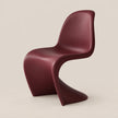 A modern sculptural chair in a deep burgundy color, shown from a three-quarters angle against a solid light beige background.