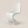 A modern white molded plastic chair with a curved, sculptural design, shown against a solid light beige background.