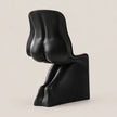 A modern sculptural black chair with an abstract, organic form, photographed against a solid, warm off-white background.