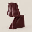 A sculptural molded chair in a deep burgundy color, photographed from the side against a solid light beige background.