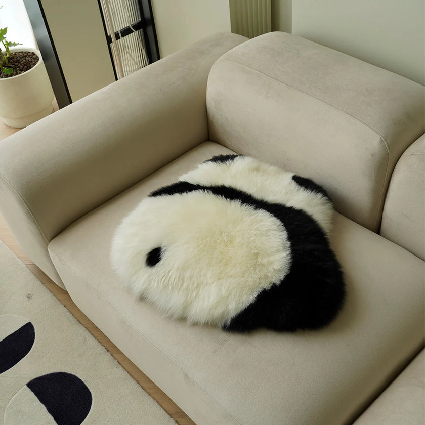 Round panda-shaped pillow on a beige sofa in a room with a plant and rug.