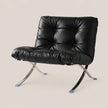 A modern black leather lounge chair with a tufted backrest and curved chrome legs, shown against a solid light beige background.