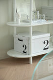 White storage boxes with the number '2' on a shelf against a light wall.