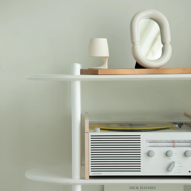 White shelf with a vintage radio, lamp, and abstract sculpture against a light green wall.