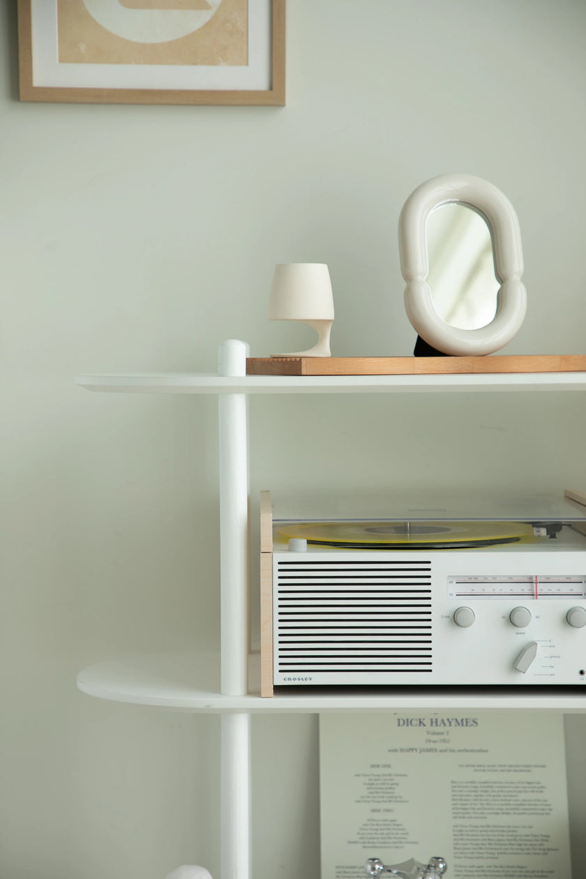 White shelf with a vintage radio, lamp, and abstract sculpture against a light green wall.
