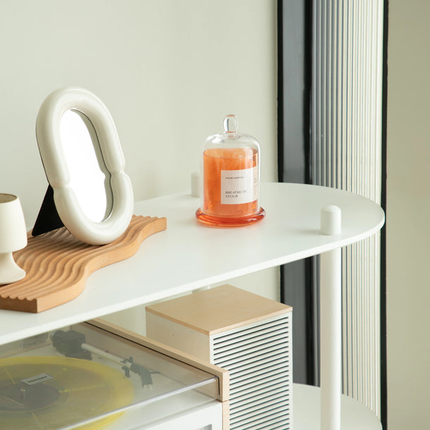 White shelf with vinyl record player, candle, and decorative items against a light wall.
