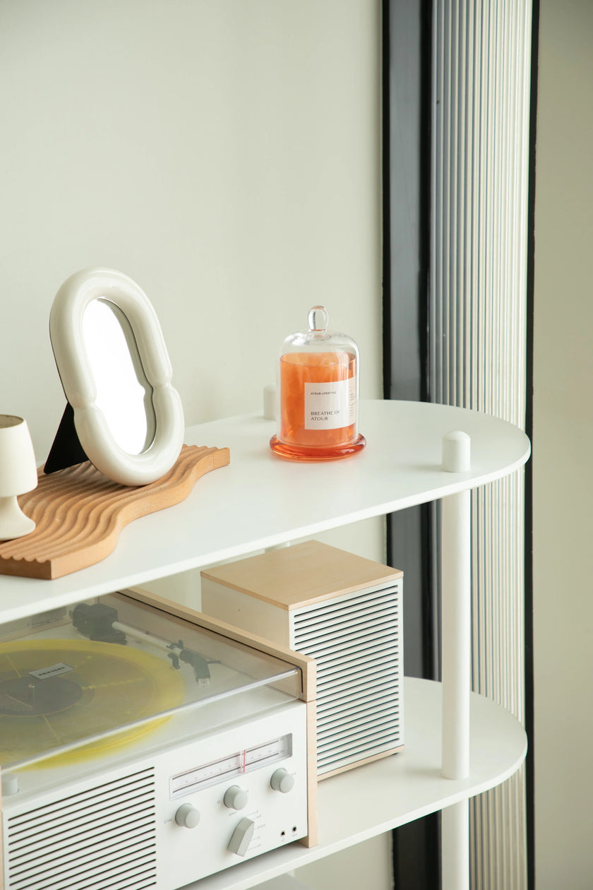 White shelf with vinyl record player, candle, and decorative items against a light wall.