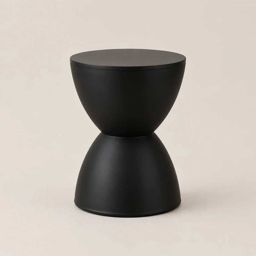 A minimalist black side table with a sculptural hourglass-like design, featuring a matte finish on a warm beige background.