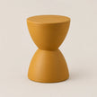 A modern, minimalist hourglass-shaped side table or stool in a matte mustard yellow finish, set against a clean, light beige studio background.