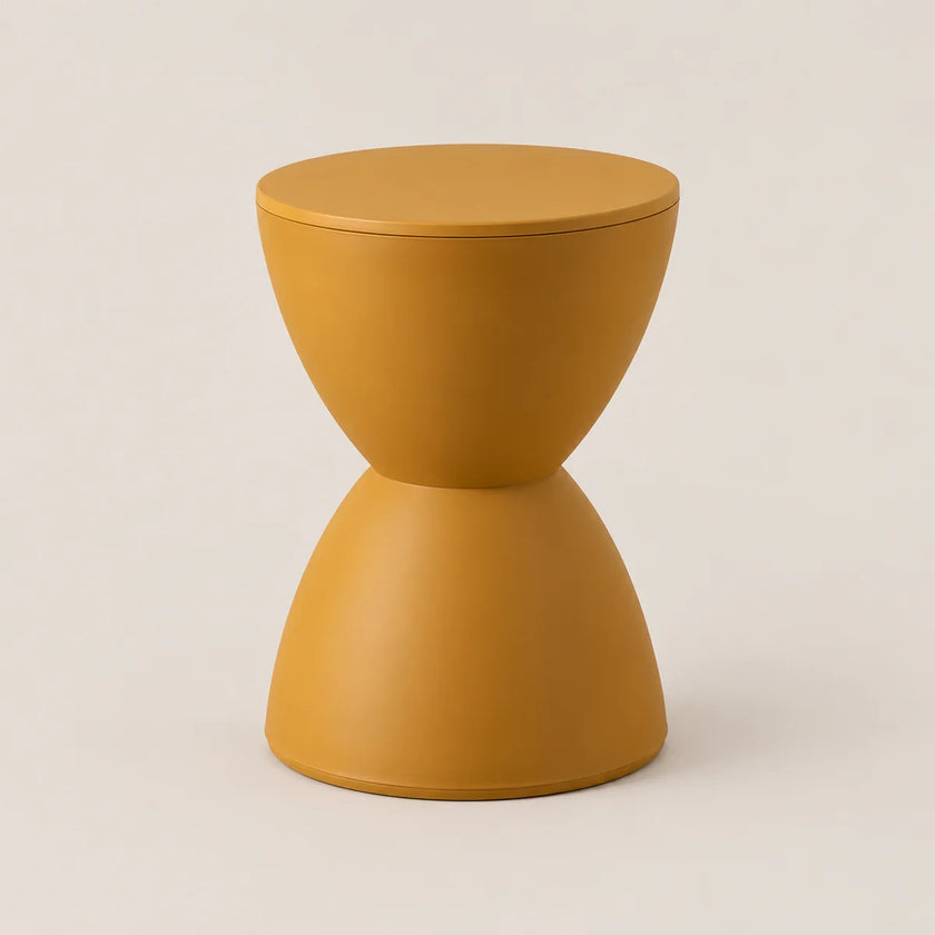 A modern, minimalist hourglass-shaped side table or stool in a matte mustard yellow finish, set against a clean, light beige studio background.
