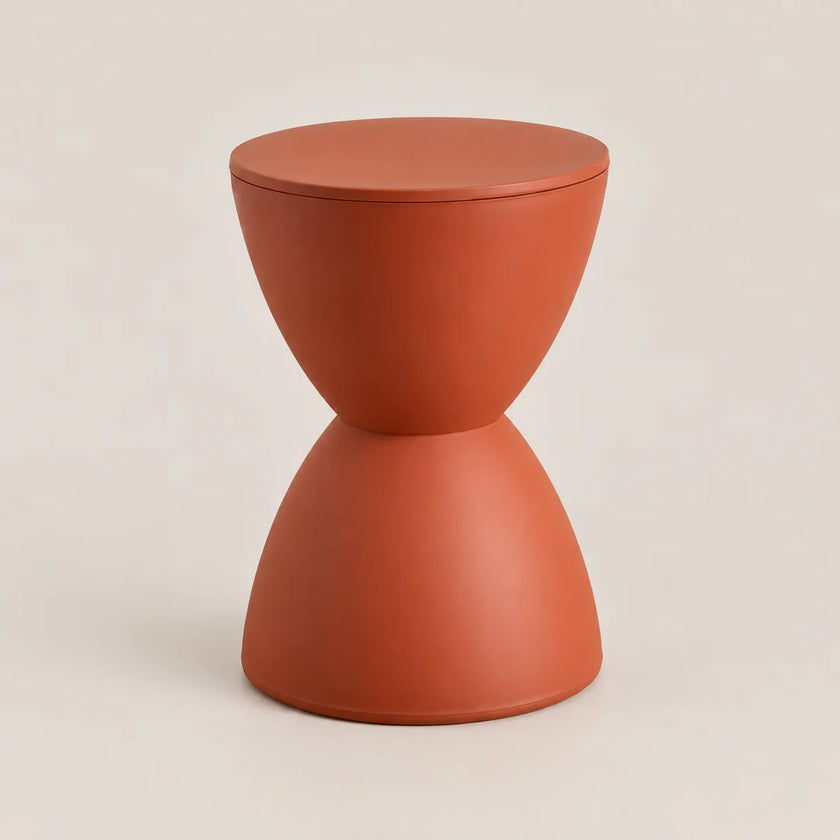 A terracotta-colored hourglass-shaped side stool with a smooth matte finish, set against a solid light beige background.