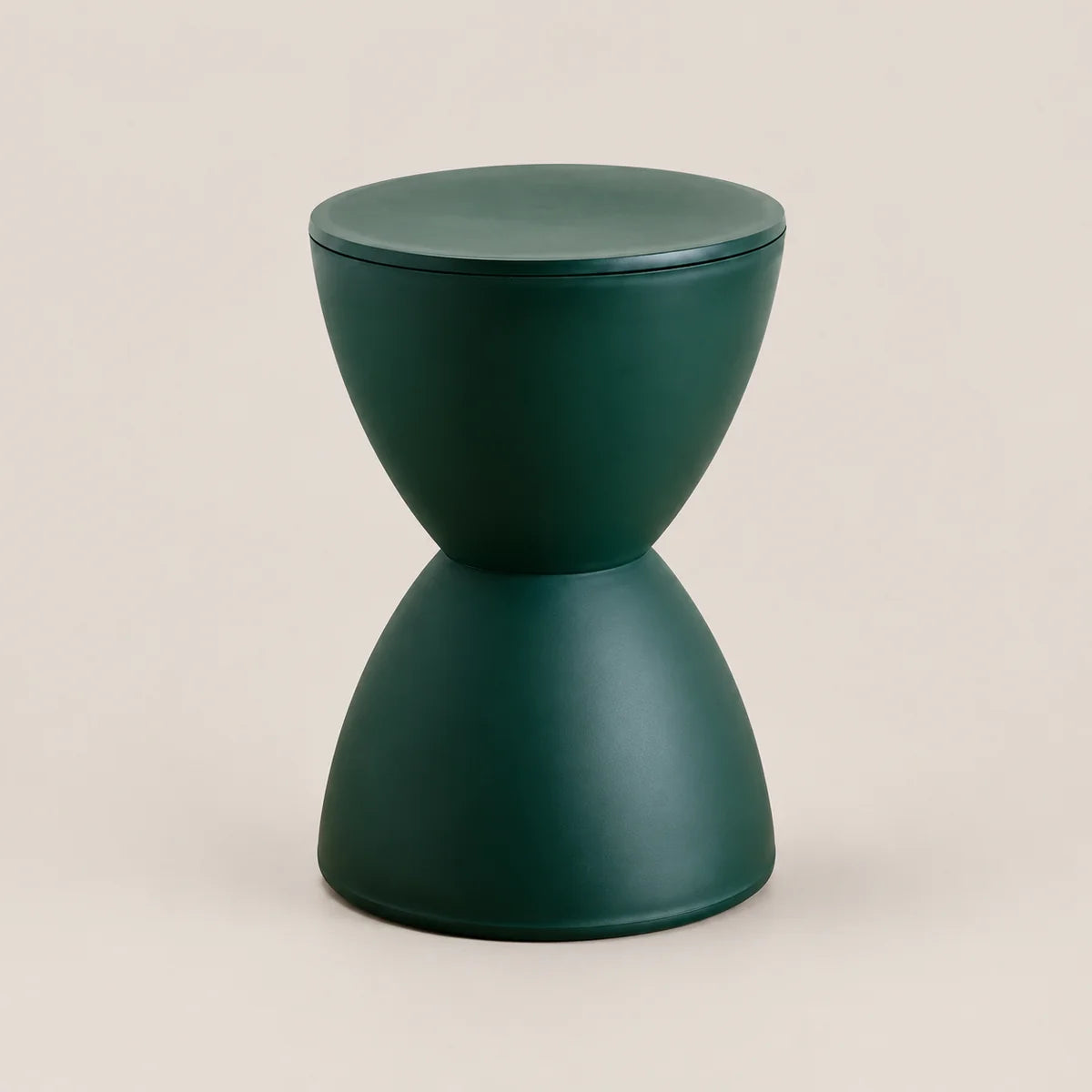 A modern dark green hourglass-shaped side table with a matte finish, set against a solid light beige background.