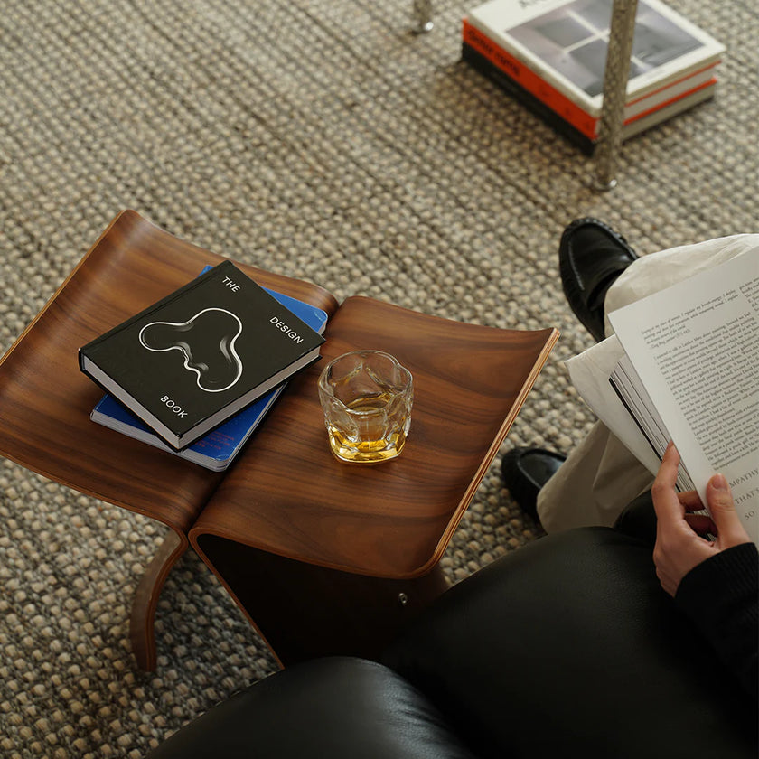 Person reading a book with a glass of whiskey on a wooden side table.