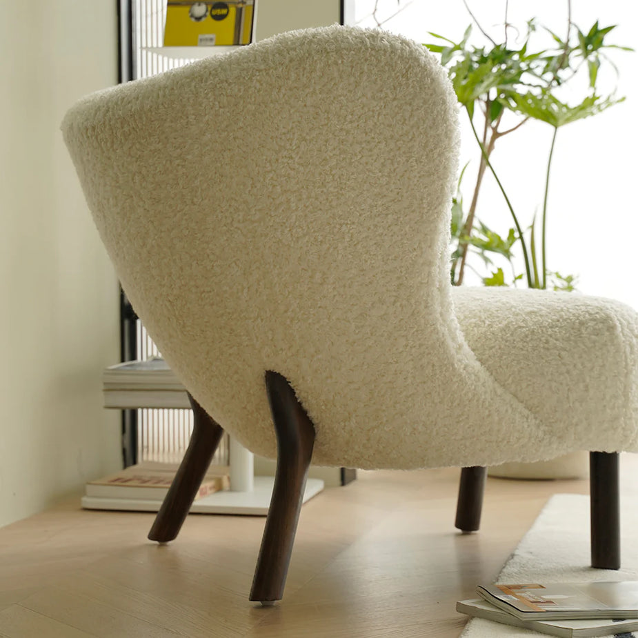 Beige textured chair with dark wooden legs in a room with a plant and books.