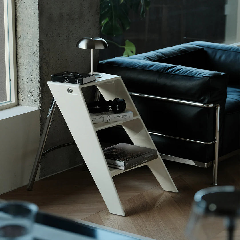 White side table with books and a lamp next to a black leather sofa.
