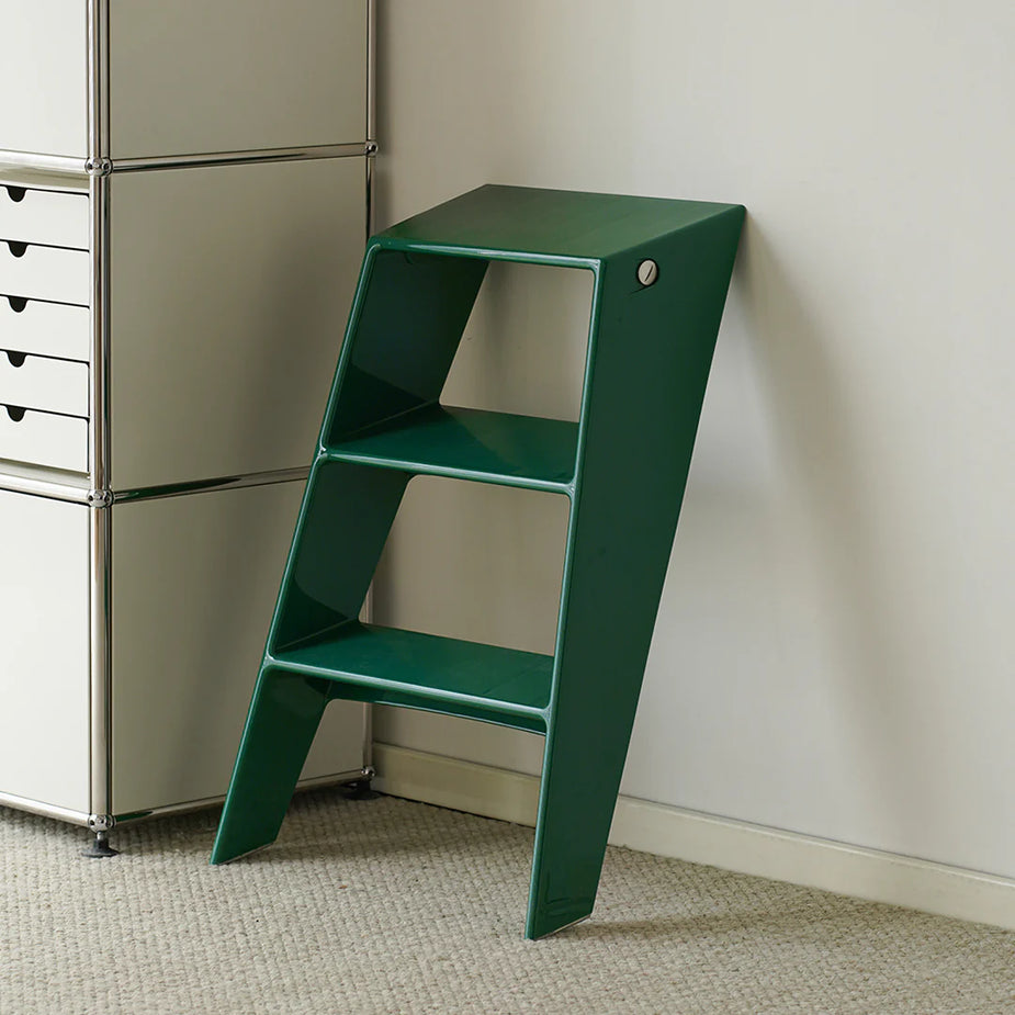 Green step ladder against a white wall with a metal cabinet in the background.